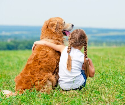 A girl hugging her dog in a field of grass