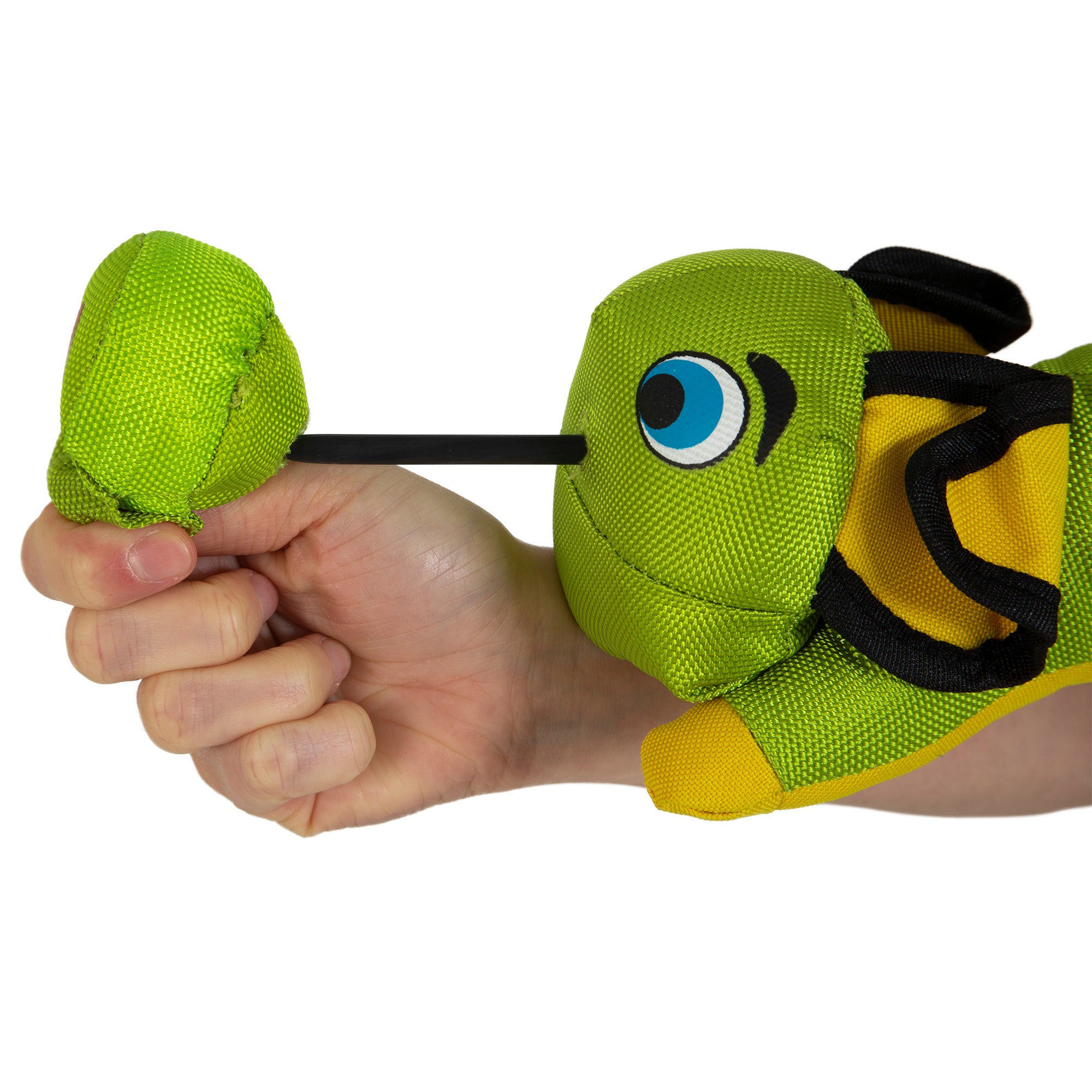 A hand holds the Hyper Pet Flying Pig Interactive Dog Toy by Hyperpet, a green and yellow fabric fish made from durable ballistic material. It has a large eye and a strap with a pull mechanism on the back, ideal for slingshot-style play.