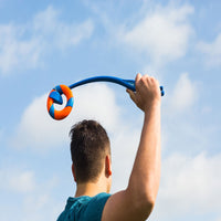 Holding the Chuckit RingChaser Dog Toy Set, a person stands ready to launch the interactive toy into the sunny, blue sky with their back facing us against a backdrop of fluffy clouds.